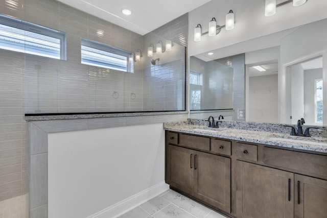 full bath featuring double vanity, marble finish floor, a walk in shower, and a sink