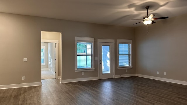 unfurnished room with dark wood-type flooring, a ceiling fan, and baseboards