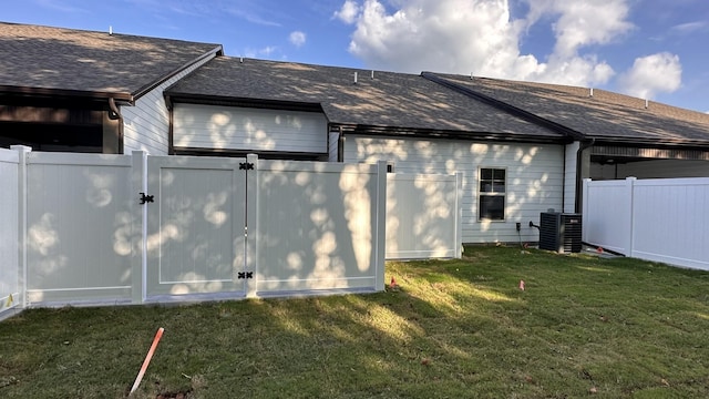 view of home's exterior featuring a shingled roof, a gate, fence, and a lawn