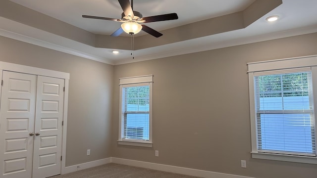 unfurnished room featuring carpet, crown molding, a raised ceiling, ceiling fan, and baseboards