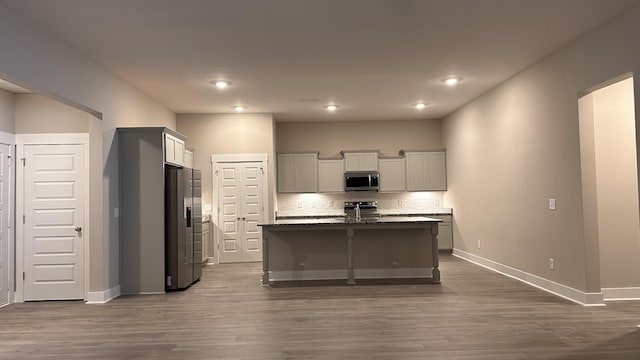 kitchen featuring a kitchen island with sink, stainless steel appliances, dark wood-style flooring, baseboards, and backsplash