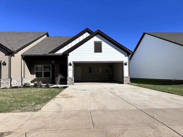 view of front of house with an attached garage, a shingled roof, stone siding, driveway, and a front yard