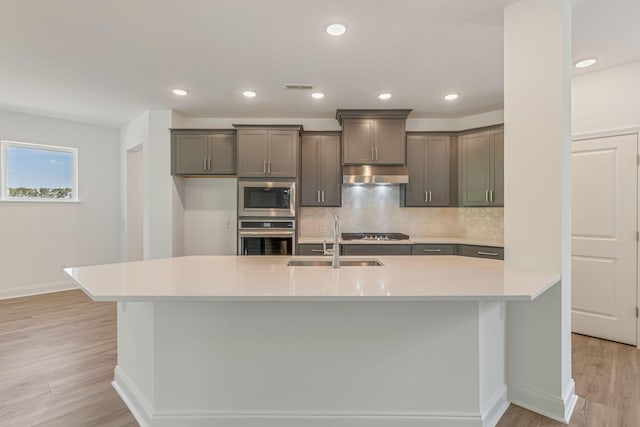 kitchen with under cabinet range hood, stainless steel appliances, a sink, visible vents, and light wood finished floors