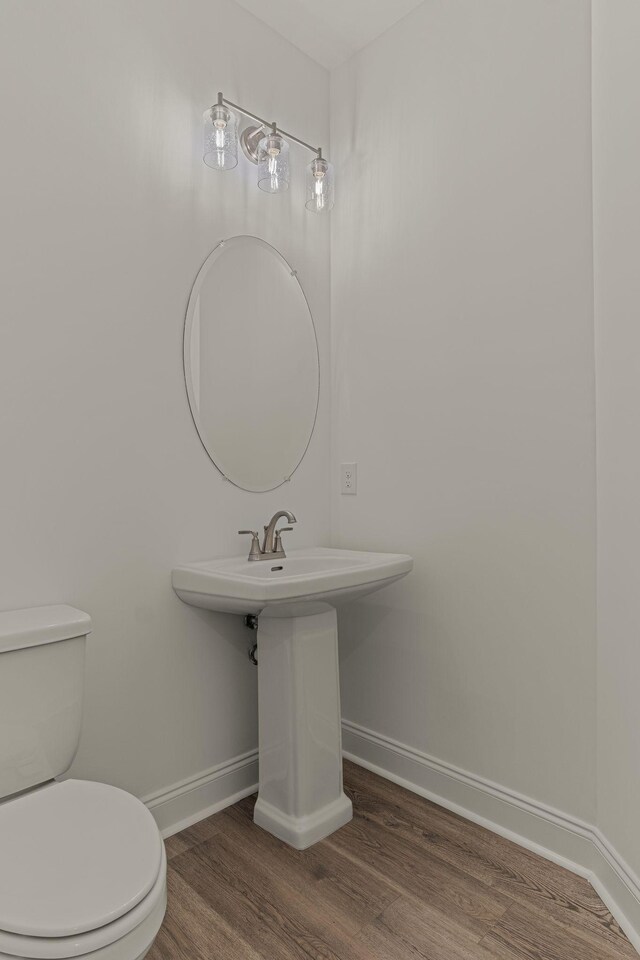 half bath featuring wood finished floors, toilet, and baseboards