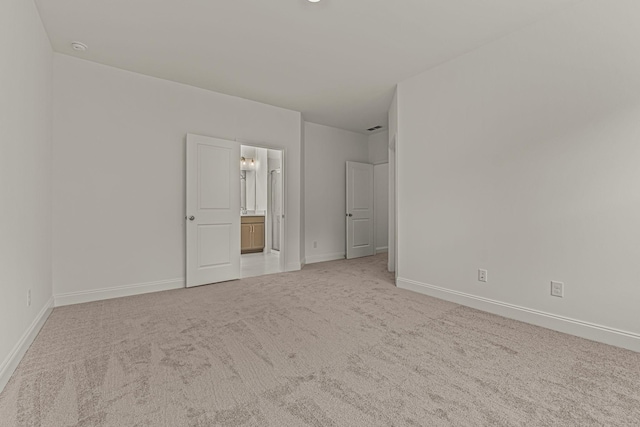 unfurnished bedroom with light carpet, baseboards, and ensuite bathroom