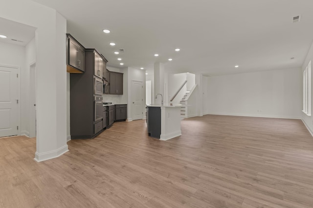 unfurnished living room with recessed lighting, light wood-style flooring, stairway, a sink, and baseboards