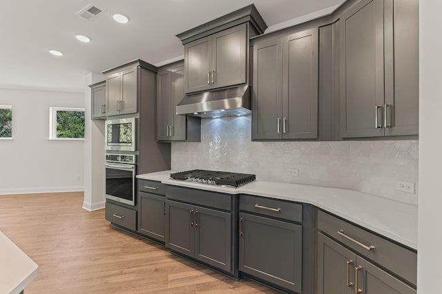 kitchen with light wood-style flooring, under cabinet range hood, visible vents, light countertops, and appliances with stainless steel finishes