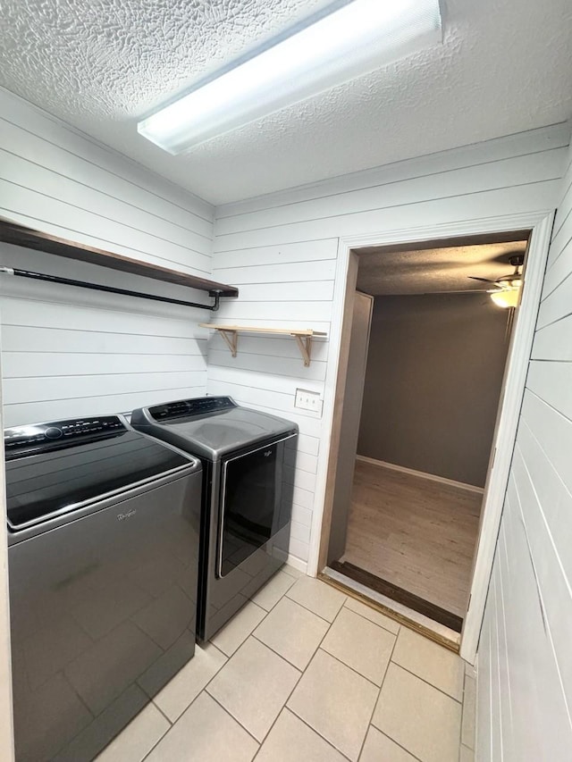 clothes washing area featuring light tile patterned floors, washing machine and dryer, wood walls, a textured ceiling, and laundry area