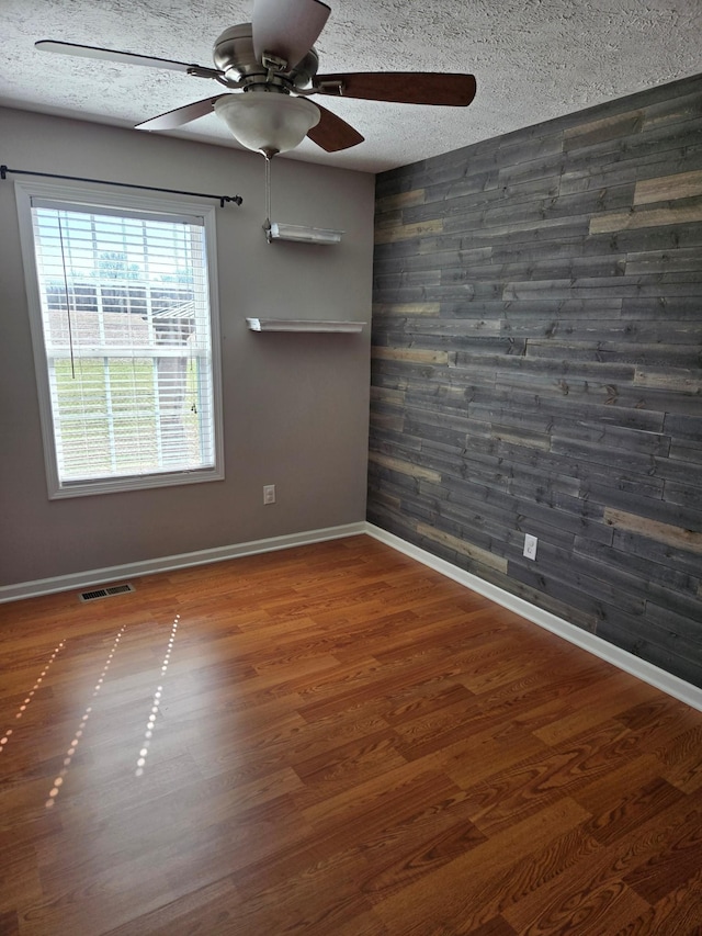 spare room with visible vents, wooden walls, a textured ceiling, wood finished floors, and baseboards