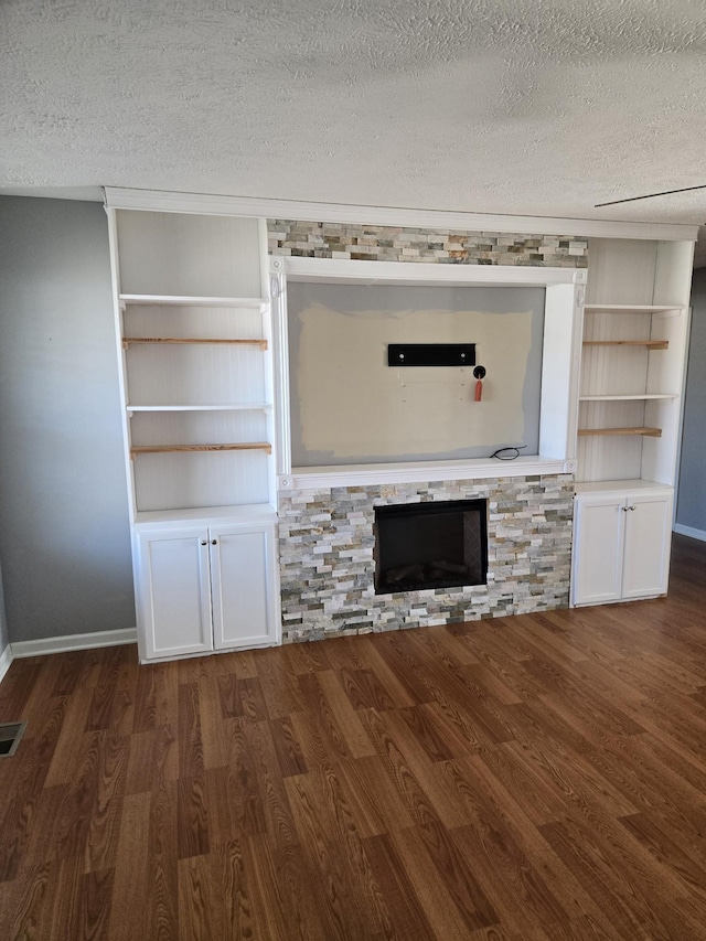 unfurnished living room with a textured ceiling, a fireplace, wood finished floors, and visible vents