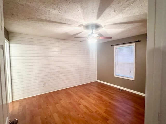 empty room with a textured ceiling, ceiling fan, wood finished floors, visible vents, and baseboards