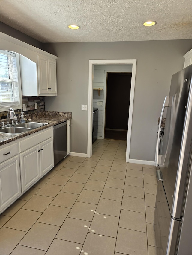 kitchen featuring light tile patterned floors, stainless steel appliances, dark countertops, white cabinetry, and a sink