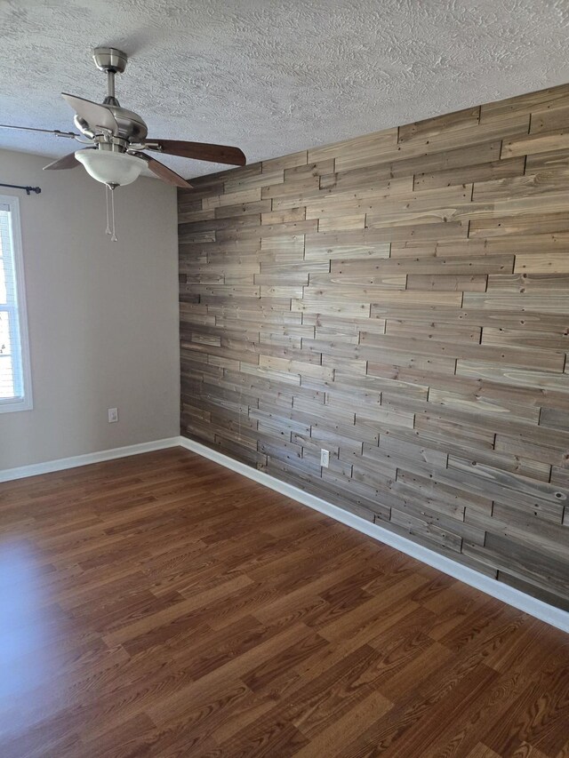 empty room featuring wood walls, a textured ceiling, baseboards, and wood finished floors