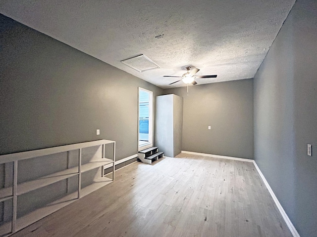 unfurnished room with ceiling fan, baseboards, attic access, wood finished floors, and a textured ceiling