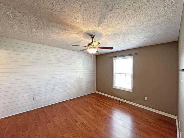 unfurnished room with visible vents, a ceiling fan, a textured ceiling, wood finished floors, and wooden walls