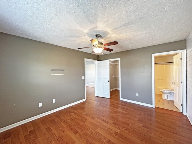 unfurnished bedroom with a walk in closet, baseboards, wood finished floors, a closet, and ensuite bath