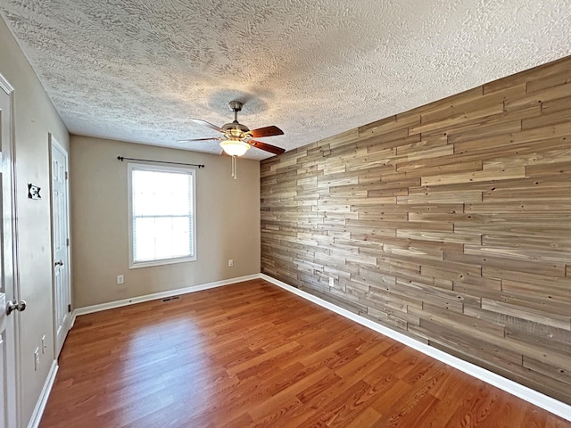 empty room with wooden walls, baseboards, ceiling fan, wood finished floors, and a textured ceiling