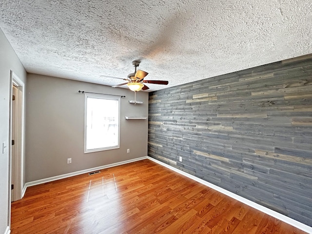 unfurnished room featuring a textured ceiling, an accent wall, ceiling fan, and wood finished floors