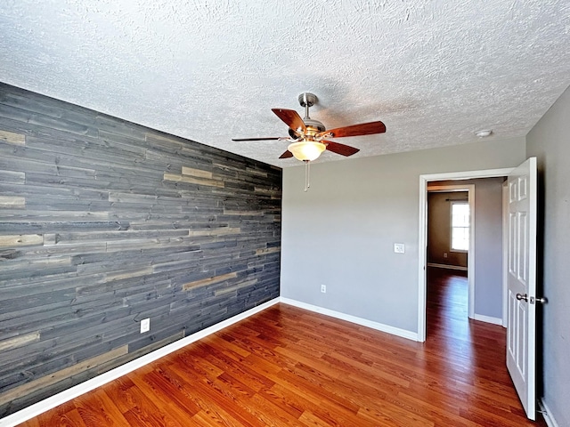 empty room with a ceiling fan, wooden walls, wood finished floors, and an accent wall