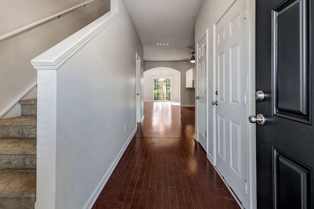 hallway featuring arched walkways, dark wood-style flooring, visible vents, stairway, and baseboards