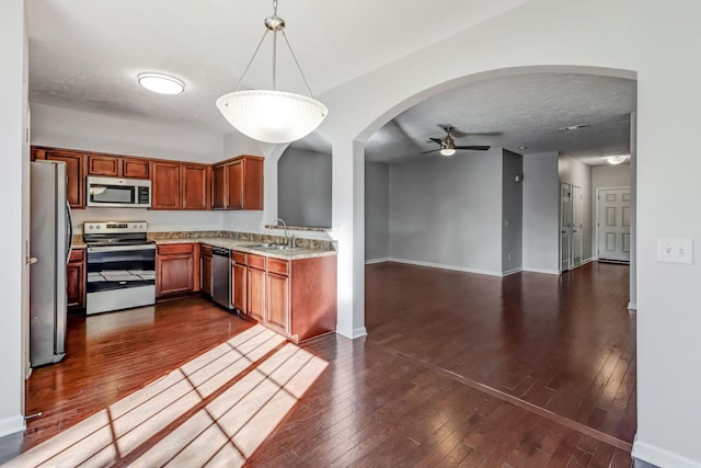 kitchen with stainless steel appliances, dark wood-style flooring, a sink, brown cabinetry, and decorative light fixtures