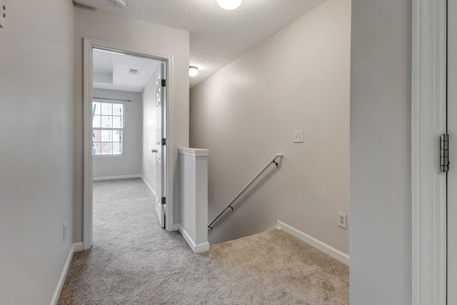 hallway with a textured ceiling, carpet floors, an upstairs landing, and baseboards