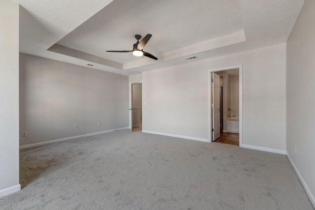 carpeted empty room featuring a tray ceiling, ceiling fan, and baseboards