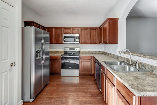 kitchen with a sink, light countertops, appliances with stainless steel finishes, brown cabinets, and dark wood finished floors