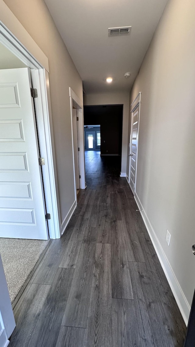 hallway featuring dark wood-type flooring, visible vents, and baseboards