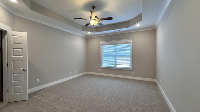 carpeted spare room featuring a tray ceiling, crown molding, visible vents, ceiling fan, and baseboards