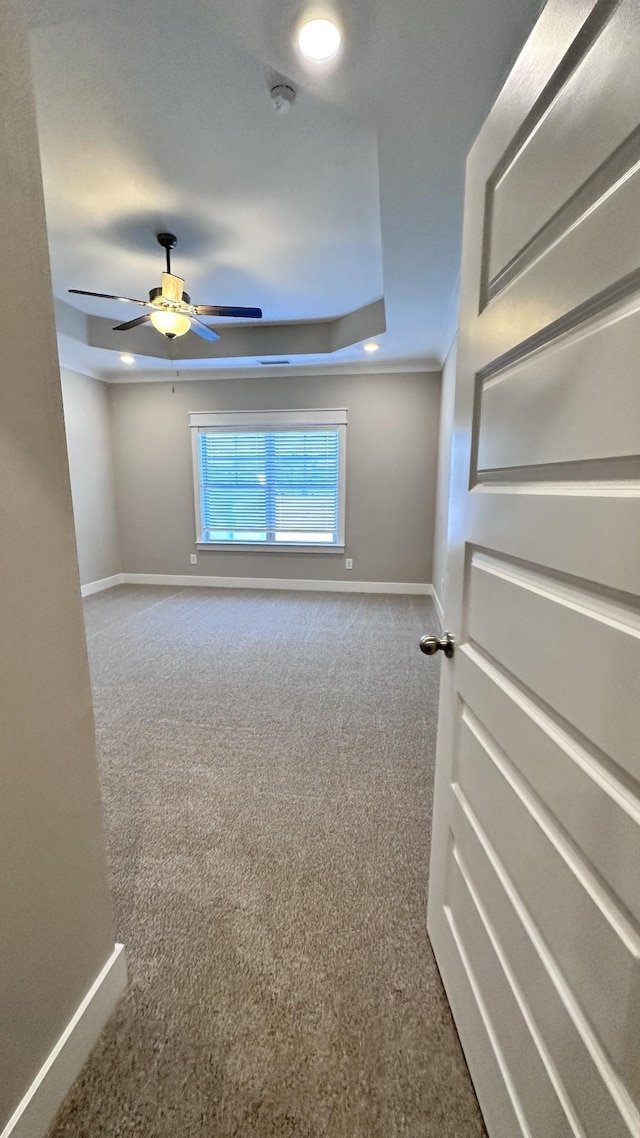 carpeted spare room with baseboards, a tray ceiling, and ceiling fan