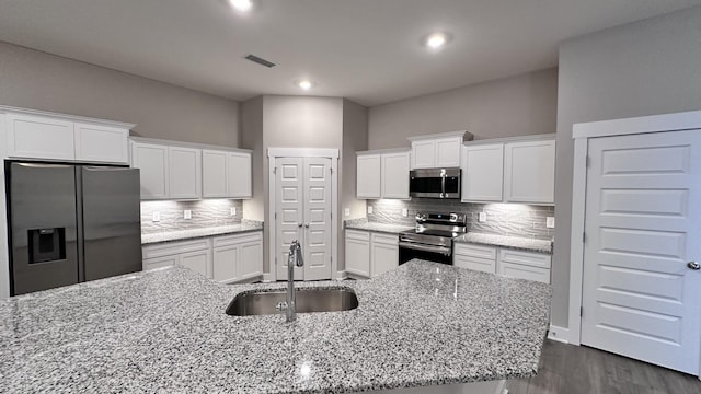 kitchen with stainless steel appliances, white cabinets, a sink, and visible vents