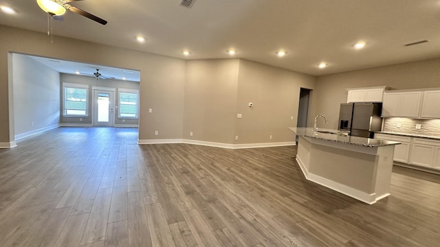 kitchen featuring stainless steel fridge, an island with sink, dark wood-style floors, open floor plan, and light stone countertops