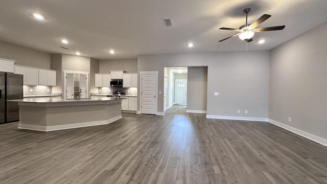 kitchen with tasteful backsplash, a center island with sink, visible vents, dark wood-style flooring, and stainless steel appliances