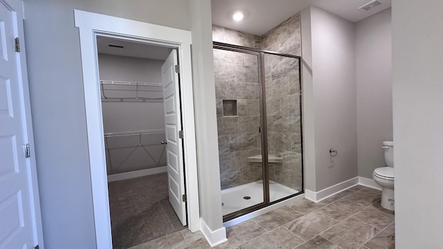 full bath with a stall shower, baseboards, visible vents, toilet, and a walk in closet