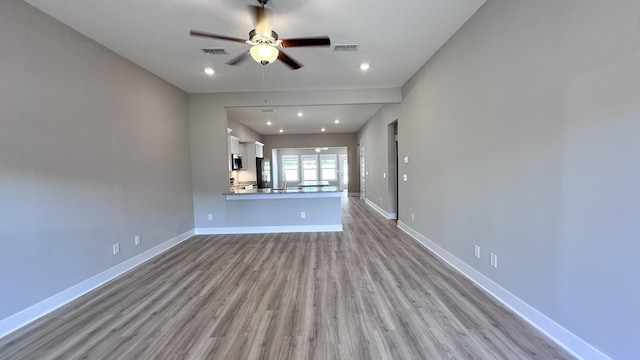 unfurnished living room featuring a ceiling fan, baseboards, visible vents, and wood finished floors