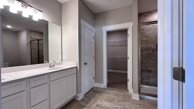 bathroom featuring double vanity, a stall shower, baseboards, a walk in closet, and a sink