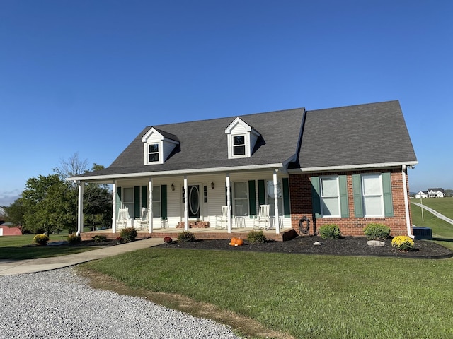 cape cod house with covered porch, a front lawn, central AC, and brick siding