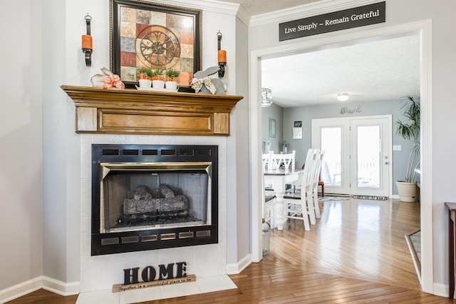 interior details featuring ornamental molding, a tile fireplace, baseboards, and wood finished floors