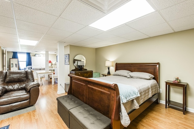 bedroom with light wood finished floors, a paneled ceiling, and baseboards