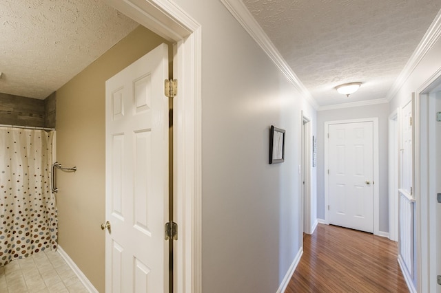 hall featuring baseboards, ornamental molding, a textured ceiling, and wood finished floors