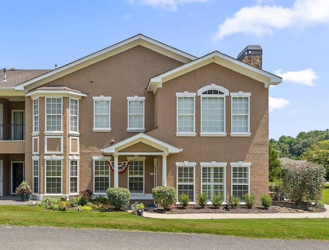 view of front facade with a front yard, a chimney, and stucco siding