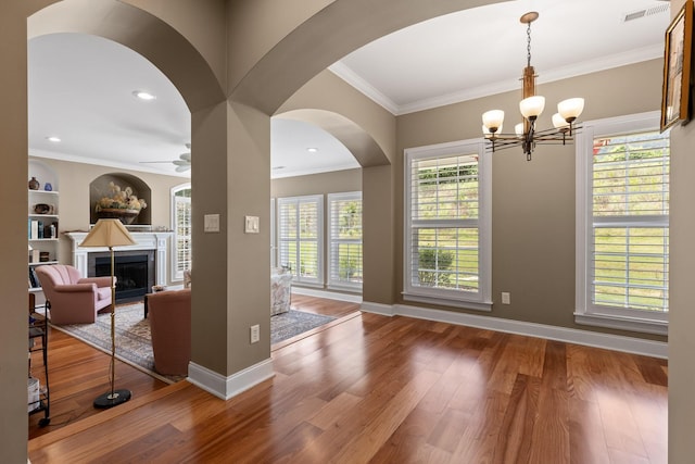 interior space with a fireplace, crown molding, visible vents, wood finished floors, and baseboards