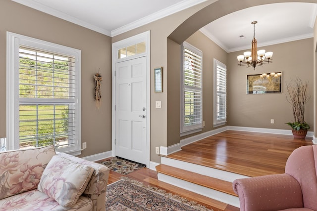 entryway featuring ornamental molding, arched walkways, wood finished floors, and a chandelier