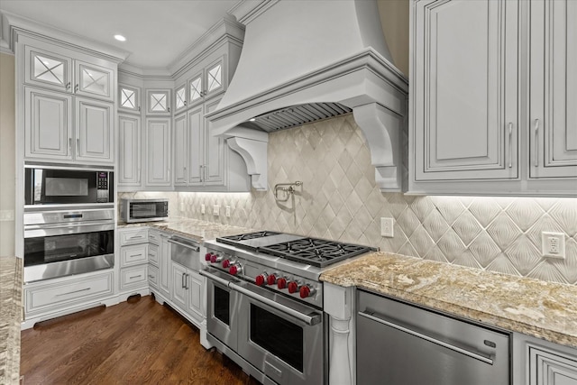 kitchen with light stone counters, stainless steel appliances, white cabinetry, backsplash, and custom range hood