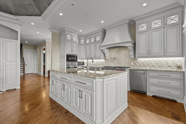 kitchen featuring dark wood finished floors, appliances with stainless steel finishes, crown molding, premium range hood, and a sink