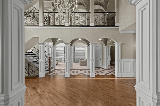 interior space with arched walkways, a decorative wall, wood finished floors, and ornate columns