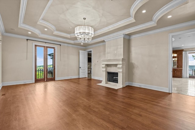 unfurnished living room featuring baseboards, wood finished floors, a tray ceiling, a chandelier, and a high end fireplace