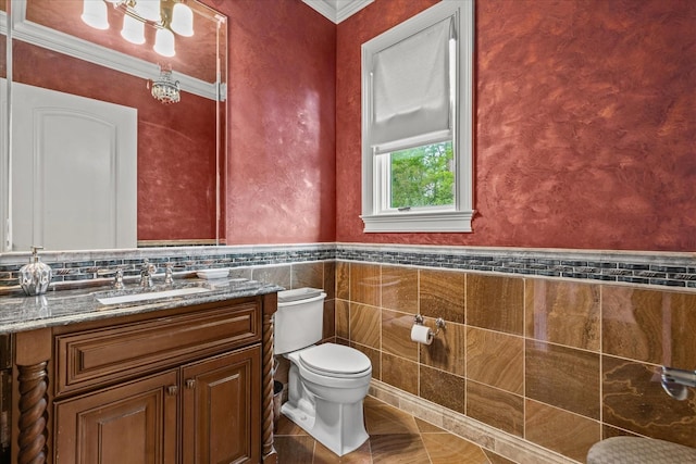 half bath with a wainscoted wall, tile walls, toilet, ornamental molding, and vanity