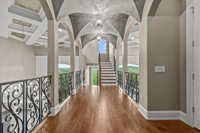 hall with a chandelier, a high ceiling, coffered ceiling, wood finished floors, and baseboards